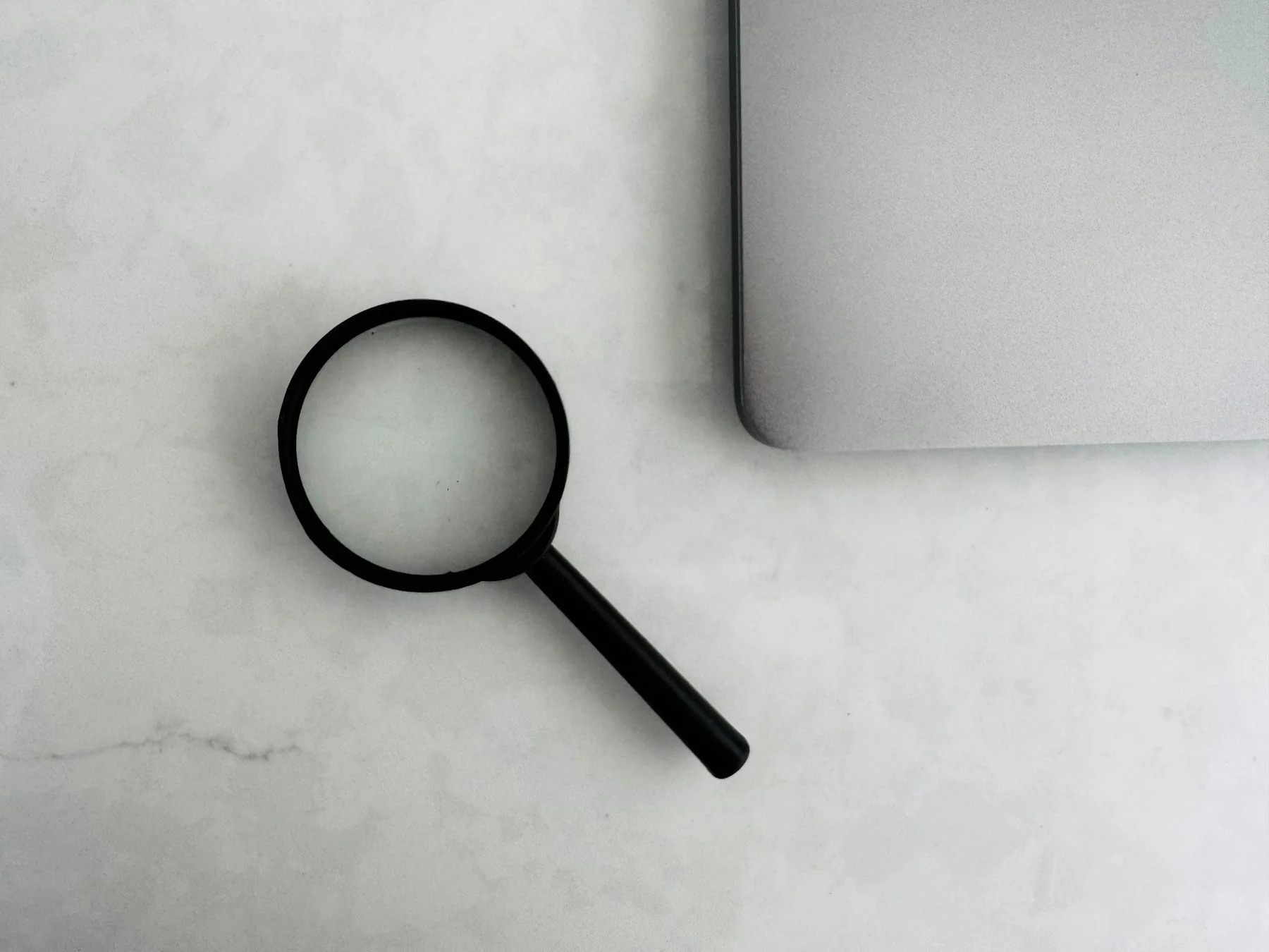 Magnifying glass resting beside a closed laptop on a white marble desk, symbolizing AI-powered search and online research