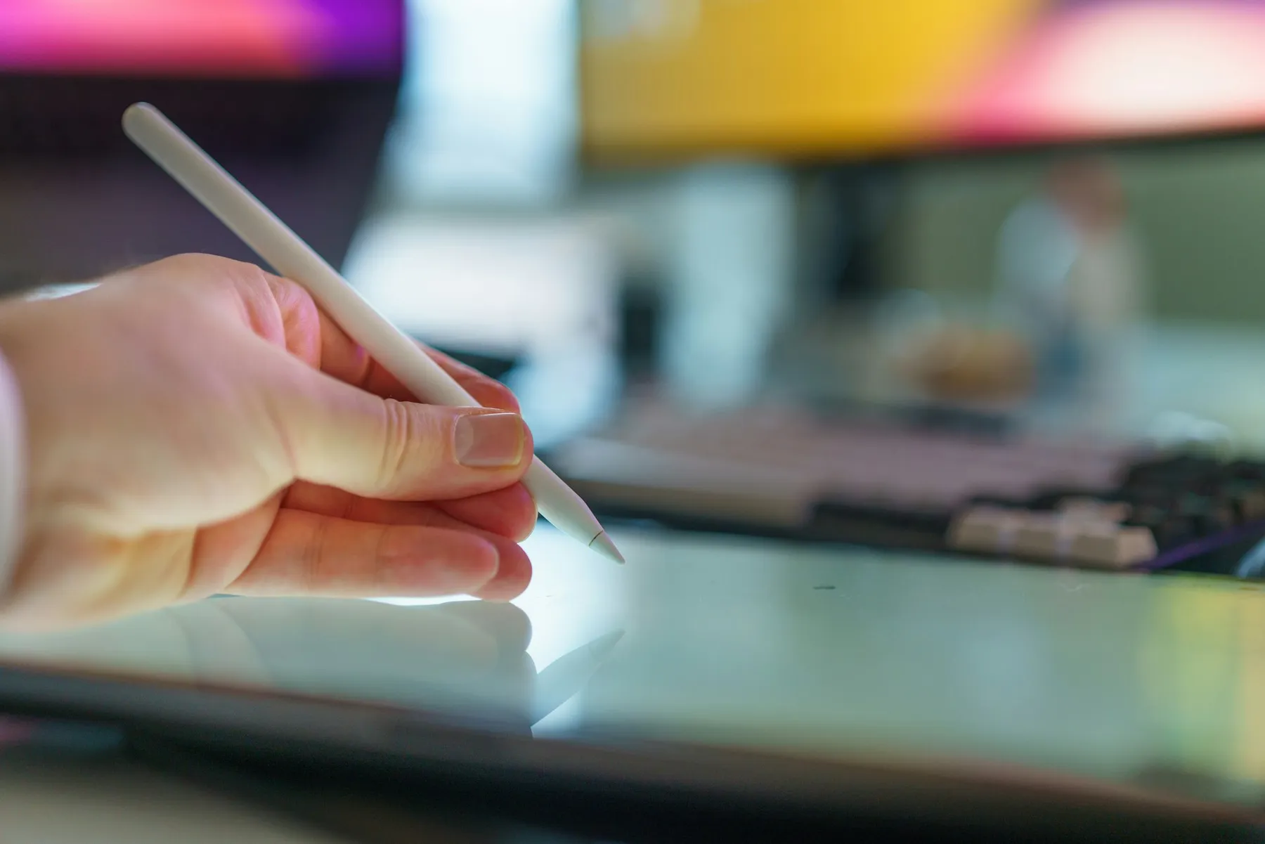 Close-up of a hand holding a digital stylus above a tablet screen, colorful bokeh lighting in the background Close-up of a hand holding a digital stylus above a tablet screen, colorful bokeh lighting in the background