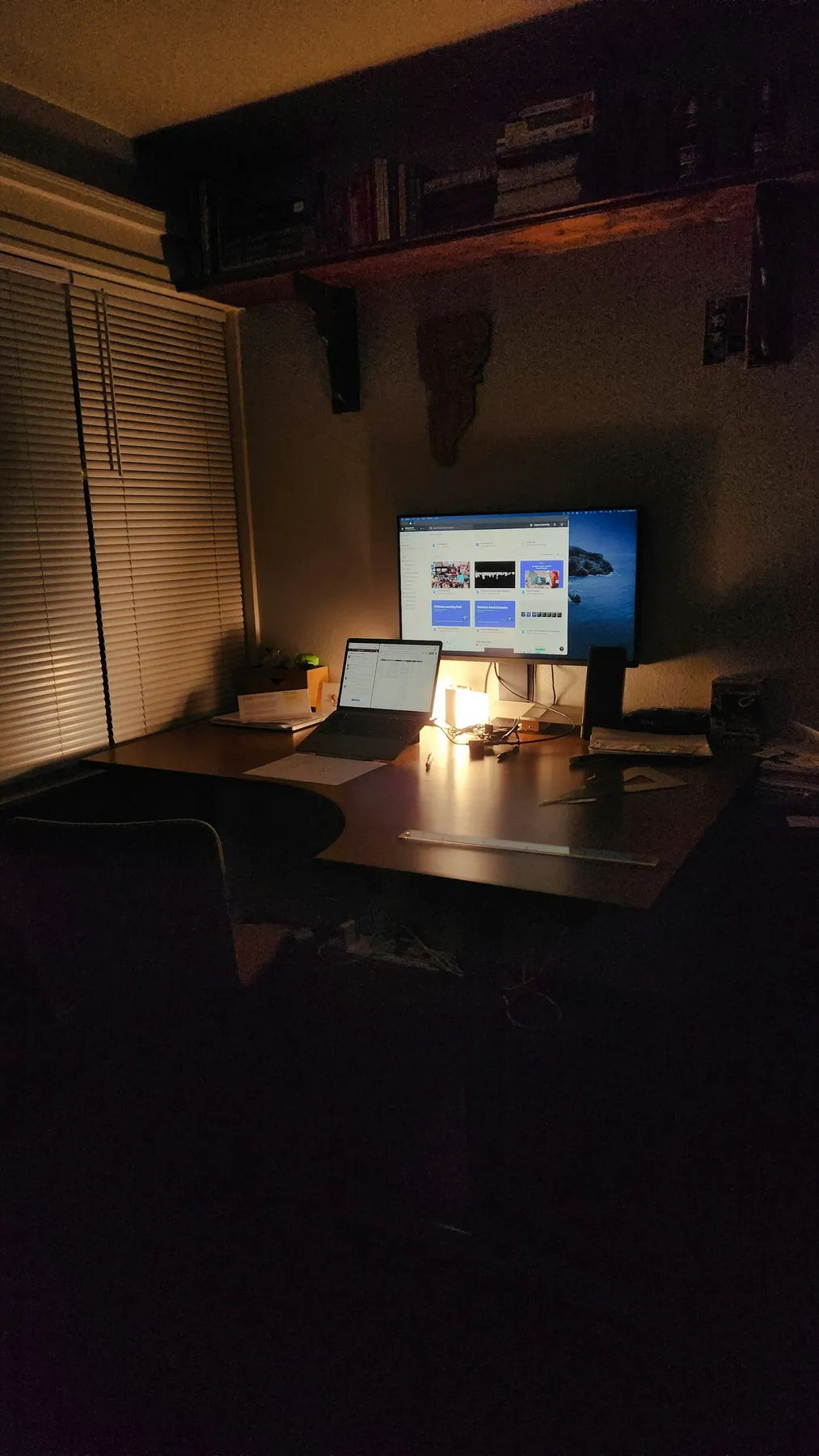 Cozy developer desk at night with laptop and monitor under warm desk-lamp lighting