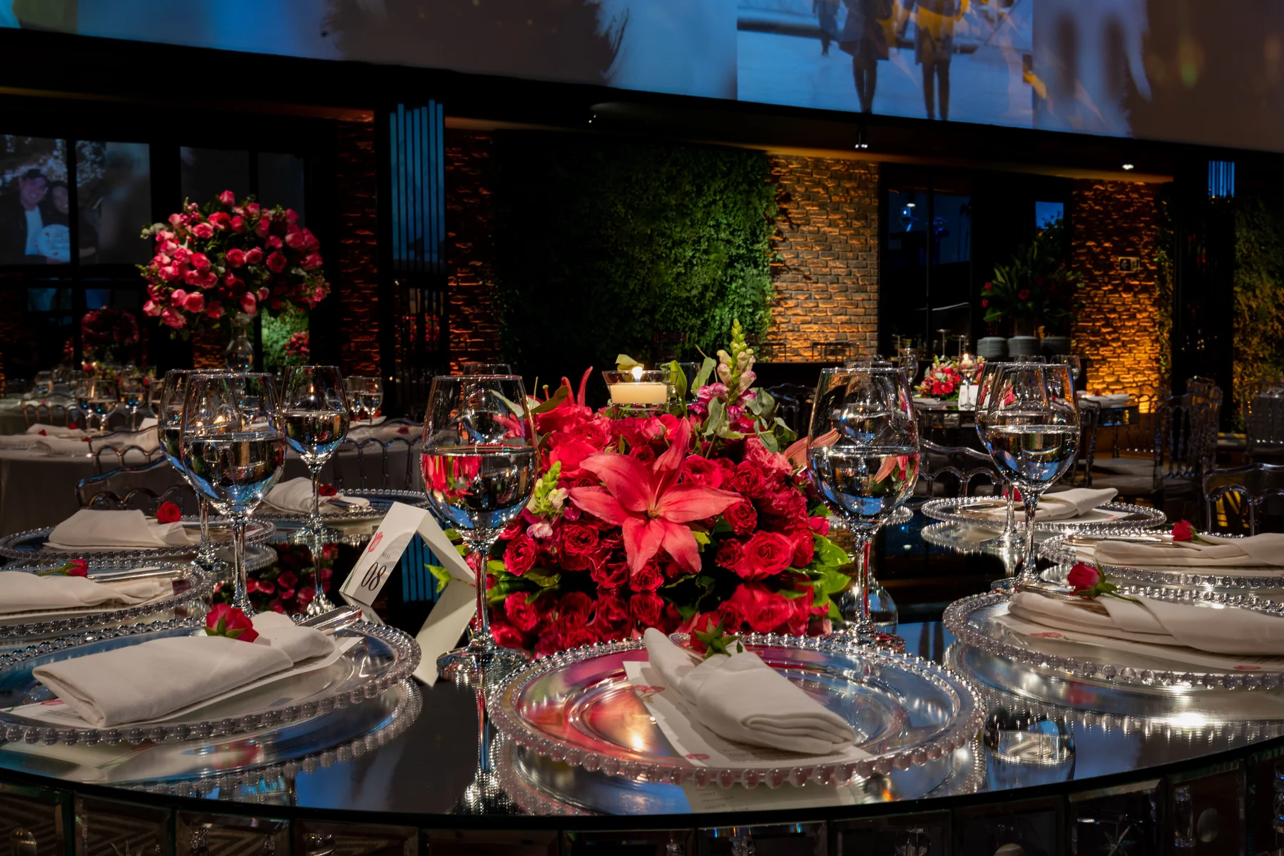 Elegant gala dinner table setting with red floral centerpieces, candlelight, and silver charger plates