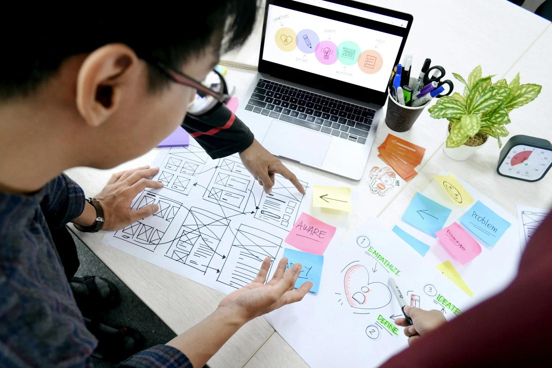 Designer sketching wireframes at a desk with a laptop