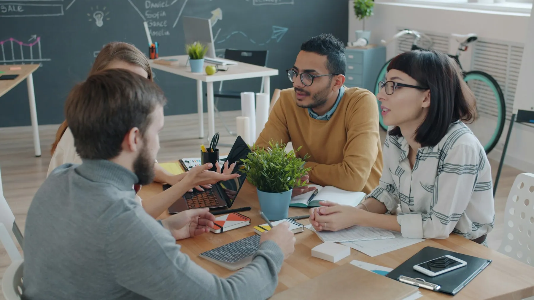 Diverse team of colleagues in a candid discussion around a laptop in a modern office Diverse team of colleagues in a candid discussion around a laptop in a modern office